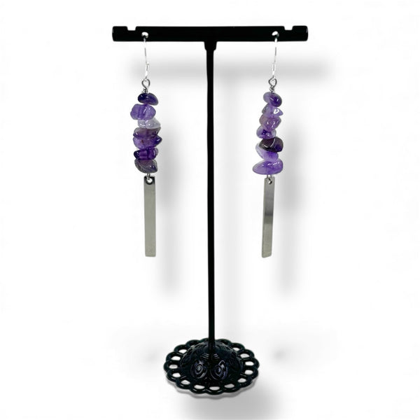 Pair of purple beaded earrings on a black stand against a white background