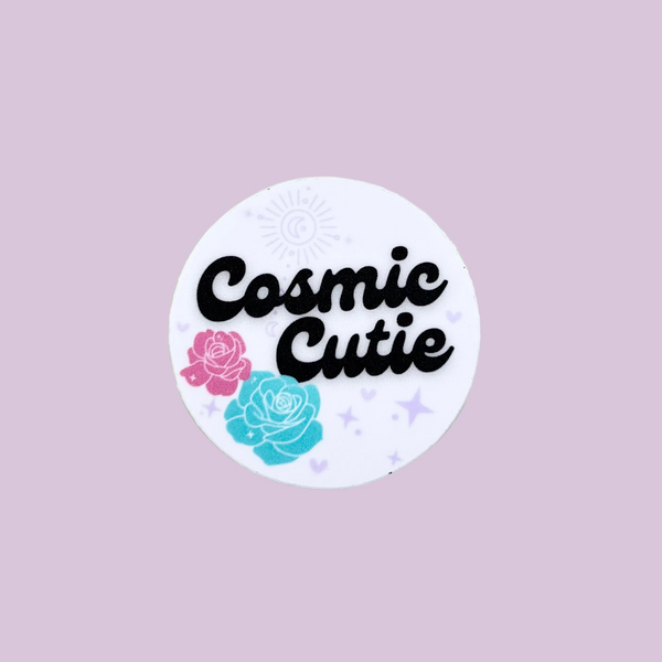 Round sticker with 'Cosmic Cutie' text and floral designs on a light gray background