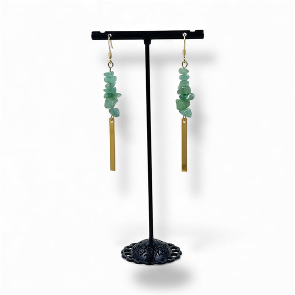 Pair of earrings with green stones and gold bars on a black stand against a white background