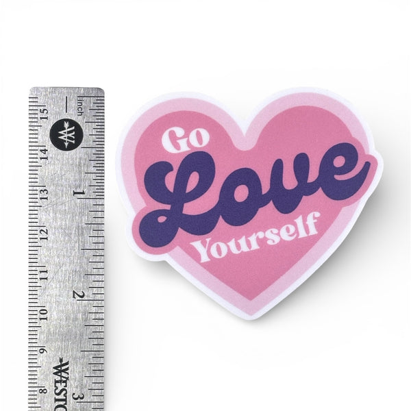 Heart-shaped sticker with 'Go Love Yourself' text next to a ruler for scale on a white background
